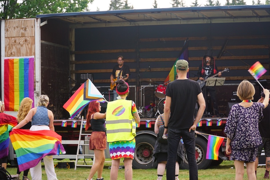 Pride Finspång. Festival i Vibjörnsparken 2022. Människor på en scen och publik framför scenen som viftar med Pride-flaggor. Foto:Stefan Gustafsson.